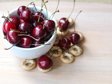 Beyaz bir fincanda olgun kirazlar ve ahşap bir arka planda simit.