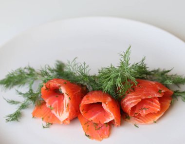 Beyaz arka planda beyaz bir tabakta somon dilimleri ve dereotları yakın plan