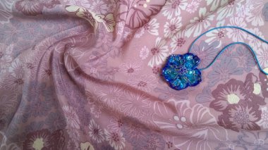Çiçek şeklinde koyu mavi kaya kristal bir kolye ile ışıldayan pembe ipek kumaş üzerinde çiçek desenli.