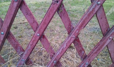 Eski kırmızı ahşap çit yıpranmış tahtalardan yapılmıştır. Oradan sararmış kuru otları olan bir çim görebilirsin..