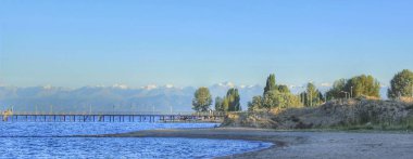 Kırgızistan doğası. Dağ sıcak göl Issyk-Kul. Sandy beach iskele ve dağlar arka planda.