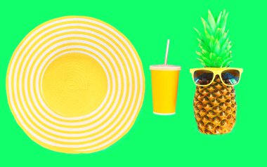 Moda ananas ile güneş gözlüğü ve sarı saman plaj şapka bardak suyu üzerinde yeşil arka plan üstten görünüm