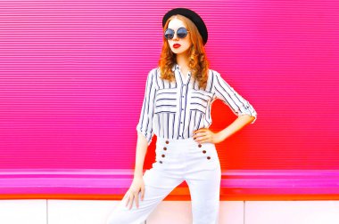Bir siyah giyen güzel bir kadın modeli pembe renkli arka plan üzerinde güneş gözlüğü beyaz pantolon şapka