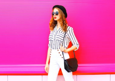 Güzel bir siyah giyen kadın şapka güneş gözlüğü beyaz pantolon ve el çantası debriyaj pembe renkli arka plan üzerinde