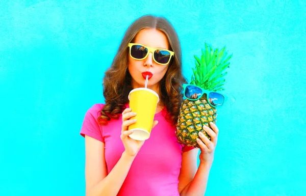 Cool girl and pineapple drinking juice from cup over colorful background