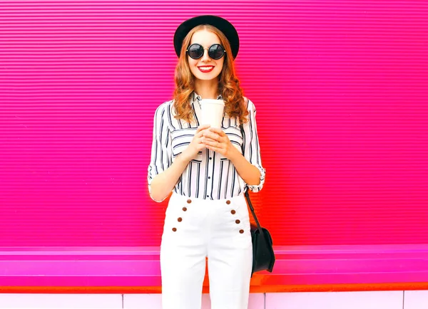 カラフルなピンクの背景にエレガントな女性のコーヒー カップを着て黒い帽子白いズボン クラッチ バッグ — ストック写真