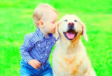 Küçük çocuk çocuk parkta çim üzerinde Golden Retriever köpek öpüyor