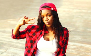 Oturan serin kız şehirde bir kırmızı kareli gömlek ve beyzbol şapkası eğleniyor