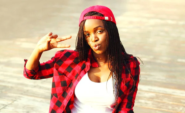 Oturan serin kız şehirde bir kırmızı kareli gömlek ve beyzbol şapkası eğleniyor