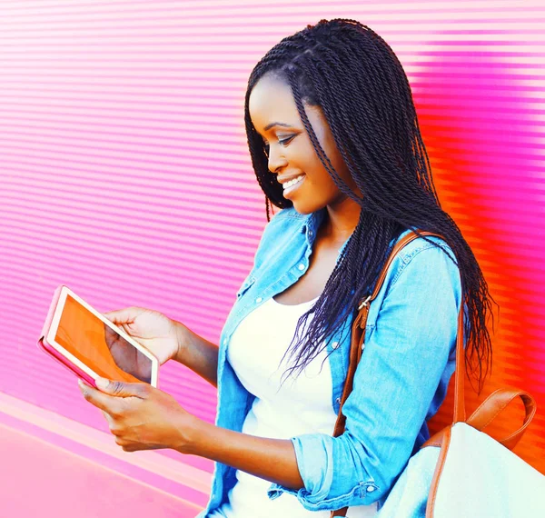 Pretty woman using tablet pc in the city over colorful pink background