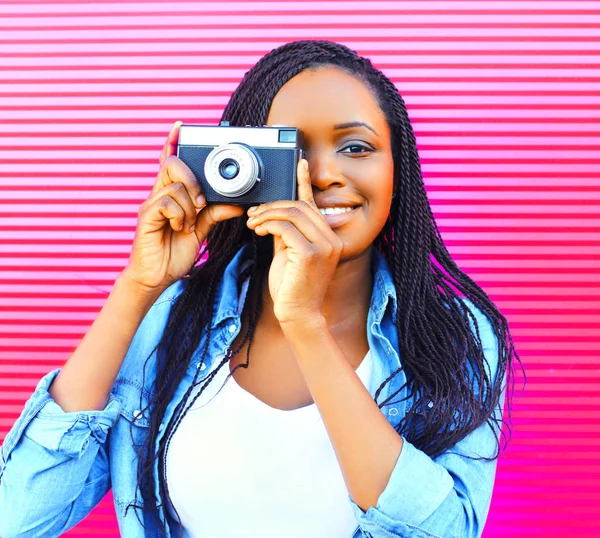 Happy african woman with old vintage camera over pink background