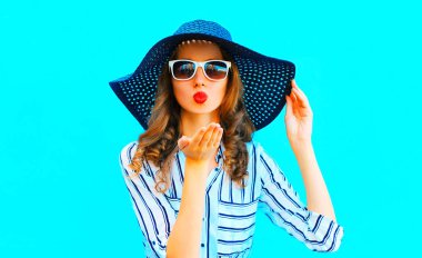 Saman yaz şapka zarif kadın mavi renkli arka plan üzerinde bir hava öpücük gönderir