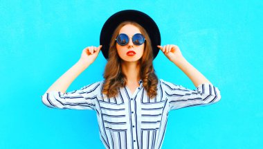 Şehirde poz mavi renkli arka plan üzerinde siyah bir şapka giyen zarif kadın