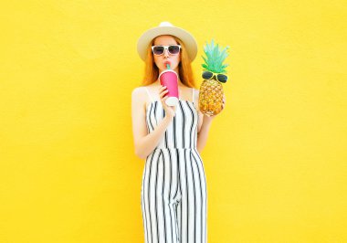 Moda güzel kadınla bir ananas suyu beyaz fincan çizgili pantolon, şapka sarı zemin üzerine yuvarlak