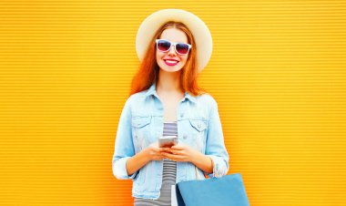 Mutlu serin kız smartphone şehrin turuncu bir arka plan üzerinde kullanıyor