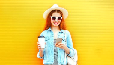 Bir akıllı telefon kullanan serin mutlu kız kahve fincanı turuncu bir arka plan üzerinde tutar