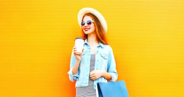 Bir fincan kahve, alışveriş torbaları turuncu arka plan üzerinde bir hasır şapka ile serin kız