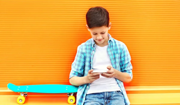 Fashion Teenager Boy Uses Smartphone Skateboard Colorful Orange Background — Stock Photo, Image