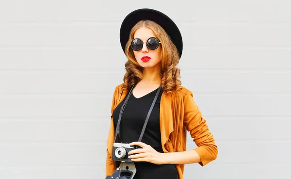 酷女孩模型与复古电影相机穿着优雅的帽子 棕色夹克摆在室外城市灰色背景 — 图库照片