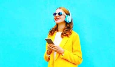 mutlu gülümseyen kadın Smartphone kullanarak portre renkli mavi arka plan üzerinde kulaklık müzik dinler