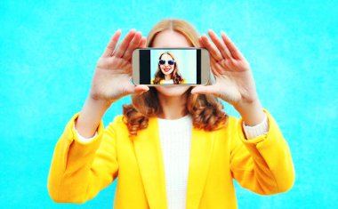 gülümseyen kadın alır bir resim akıllı telefon yakın çekim mavi renkli arka plan üzerinde kendi kendine portre