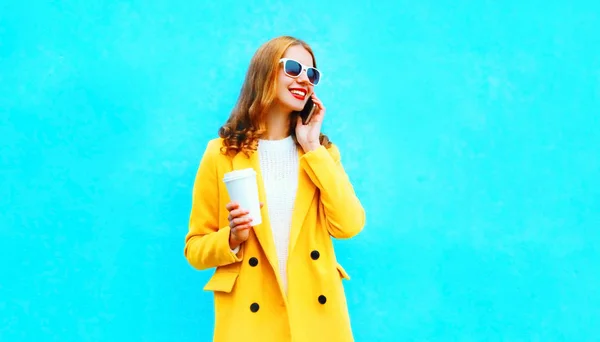 カラフルな青の背景にコーヒーのカップを保持するファッション スマート フォンで女の話が笑みを浮かべて肖像画 — ストック写真