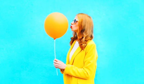 profile happy woman kisses an air balloon in yellow coat on blue background