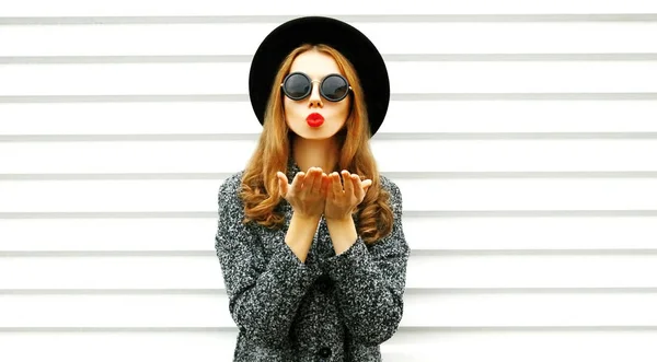 ファッション ポートレート女性が白い壁の背景に黒い丸い帽子で空気キスを送信します — ストック写真