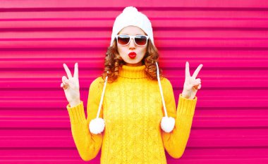 Serin kız pembe arka plan üzerinde renkli sarı kazak örme şapka kırmızı dudaklar üfleme