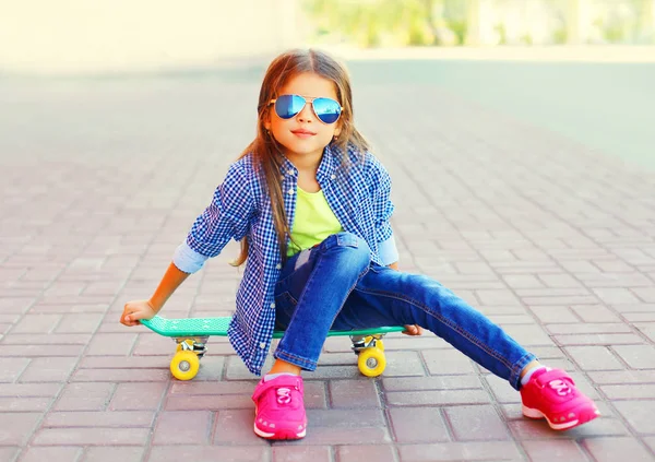 时尚的肖像微笑的小女孩坐在滑板上的城市街道 — 图库照片