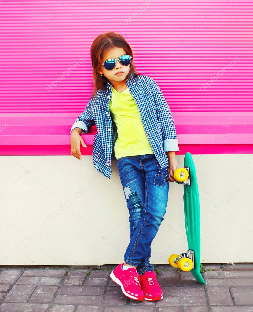 Fashion child little girl with skateboard on pink wall background