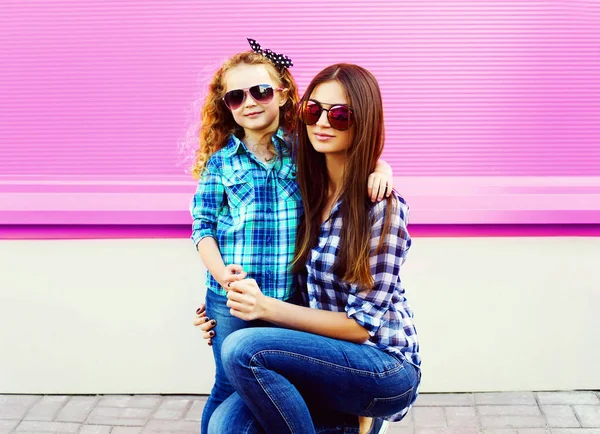 肖像母亲与女孩在格子衬衫 太阳镜在城市在五颜六色的粉红色墙壁背景 — 图库照片