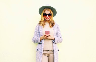 Çok gülümseyen kadın telefonu kullanarak yuvarlak şapkalı kıvırcık saçlı, duvar arka plan kat ceket