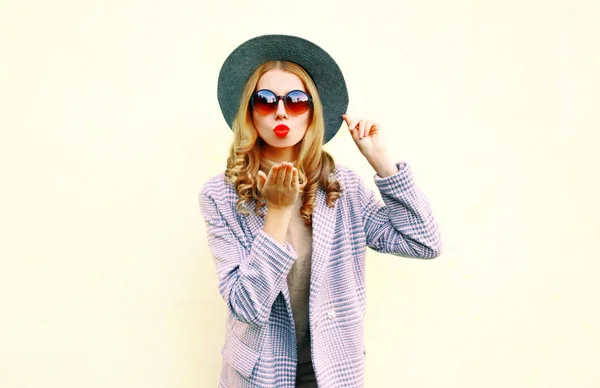 Portrait beautiful young woman blowing red lips sending air kiss in round hat on wall background