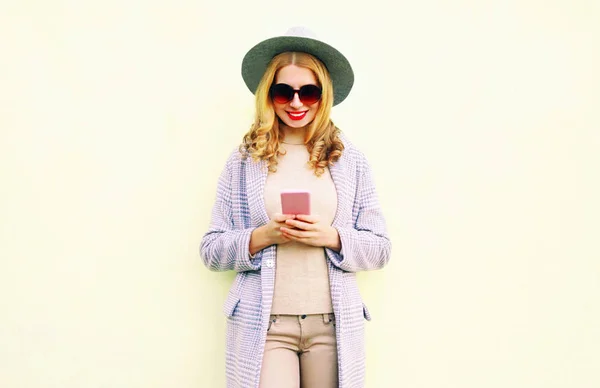 携帯電話を用いた丸い帽子の巻き毛 壁の背景にコート ジャケットかなり笑顔の女性 — ストック写真