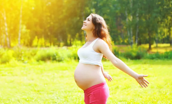 Zwangerschap concept - gelukkig lachende zwangere vrouw in park genieten van zomer — Stockfoto