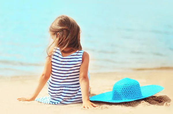 Niña niña en vestido a rayas con sombrero de paja de verano sentado —  Fotos de Stock