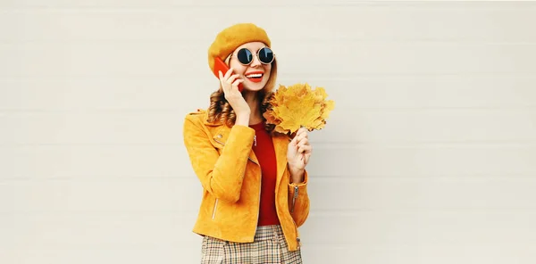 Höst porträtt leende kvinna ringer på telefon som innehar gula lönn blad klädd i franska Beret på City Street över grå vägg bakgrund — Stockfoto