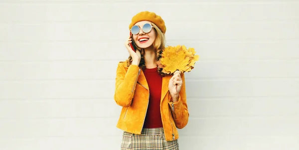 Herfst portret Glimlachende vrouw die belt op telefoon met gele esdoorn bladeren dragen Franse baret op stad straat over grijze muur achtergrond — Stockfoto