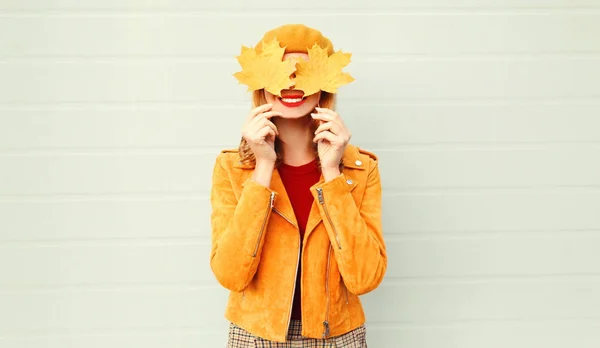 Осінній настрій! щаслива усміхнена жінка тримає в руках жовте кленове листя, приховуючи очі на сірому фоні стіни — стокове фото