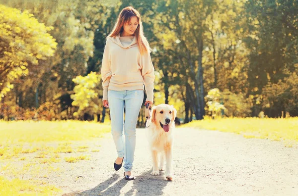 Jovem mulher andando com seu cão Golden Retriever na trela no dia ensolarado de outono — Fotografia de Stock