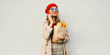 Güzel, gülümseyen bir kadının portresi. Elinde alışveriş poşeti ve üzerinde beyaz ekmek ekmeği olan boş gri duvar arkaplanı var.