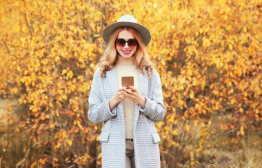 Sonbahar portresi, mutlu, mutlu, gülümseyen bir kadın. Elinde gri bir ceket, sarı yapraklı yuvarlak bir şapka var.