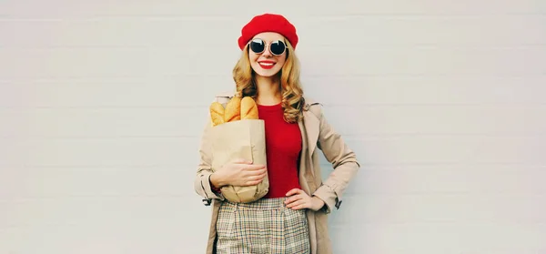 Porträtt vacker leende kvinna som håller matvaror shopping papperspåse med lång vitt bröd baguette över tom grå vägg bakgrund — Stockfoto