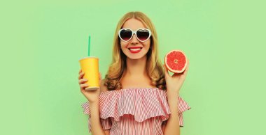 Yeşil arka planda sulu greyfurt gösteren meyve suyuyla gülümseyen genç bir kadının yaz portresi