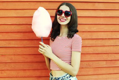 Eğlence parkında ahşap duvarda pamuk şekerle gülümseyen genç bir kadının yaz portresi.