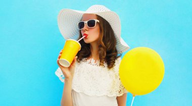 Güzel bir genç kadın portresi. Sarı balonla taze meyve suyu içiyor. Mavi arka planda yaz hasır şapkası takıyor.