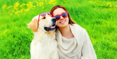 Parkta yeşil çimlerde güneş gözlüğü takan Golden Retriever köpeğiyle portre kızı.