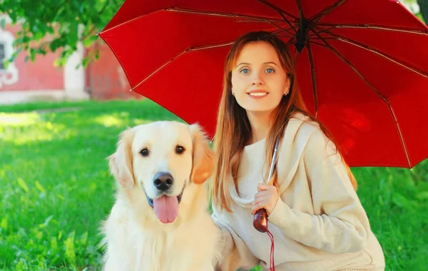 公園内の芝生の上に赤い傘の下に一緒に隠れてゴールデンレトリバー犬と肖像画の所有者の女性 — ストック写真