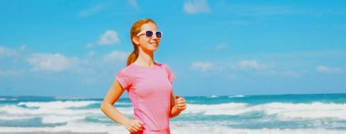 Genç bir kadın deniz kenarında sahilde koşuyor.